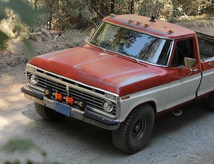 Vintage red and white Ford pickup on a dirt road with bumper-mounted SlimLite 6” LED lights for off-road visibility.